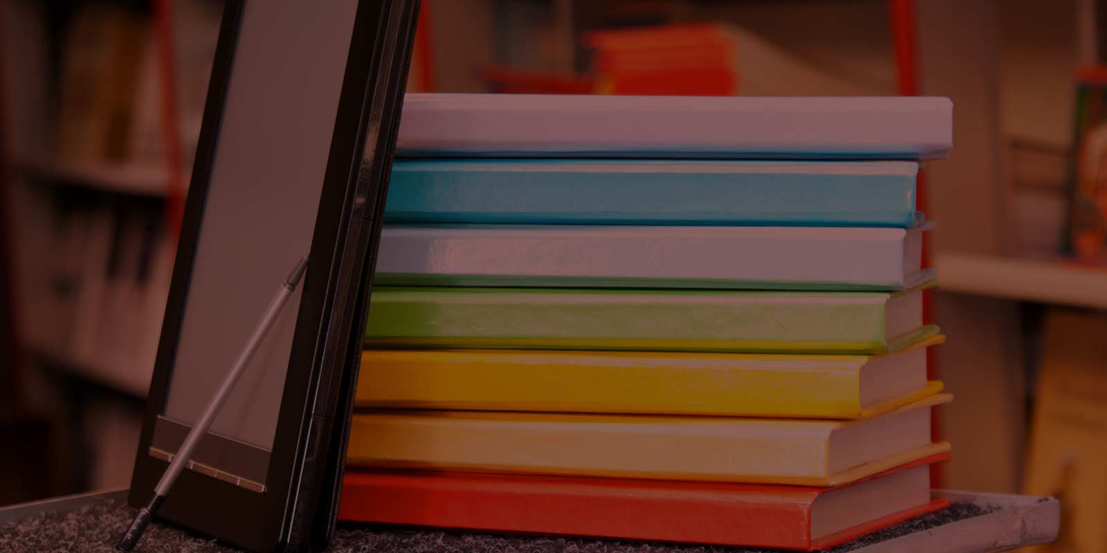 Some blank books with a tablet and stylus in front, books have no writing on the spine, they are colourful